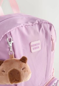 Light purple backpack with pink straps and a small plush bear keychain hanging from a side zipper pull.