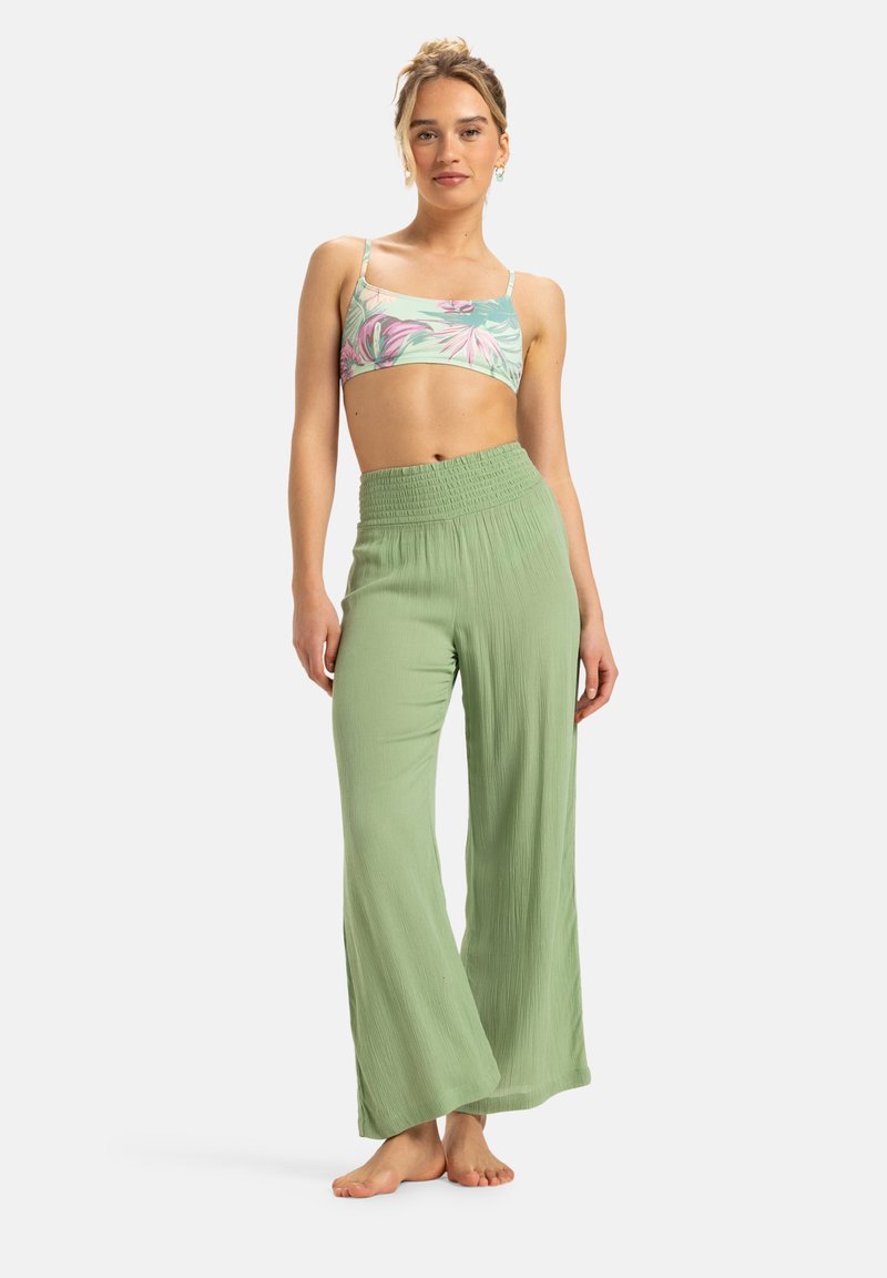 Lichtgroene, wijde broek met een gestructureerde afwerking en een elastische tailleband, gecombineerd met een bloemenpatroon crop top in pastelkleuren.
