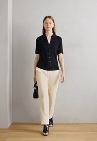 Camicia nera a maniche corte con bottoni, abbinata a pantaloni beige chiaro larghi e stivali neri lucidi. Borsa nera con dettagli bianchi.
