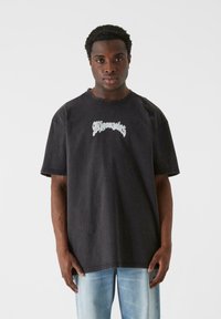 Sort oversized t-shirt lavet af bomuld, med korte ærmer, rund hals og hvid grafisk tekst på tværs af brystet, parret med lyse jeans.