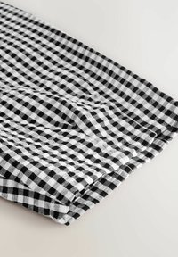 Tissu à carreaux noir et blanc, plié, présentant un motif en grille avec de petits carrés. Tissage léger et texturé visible. Matériau en coton doux.