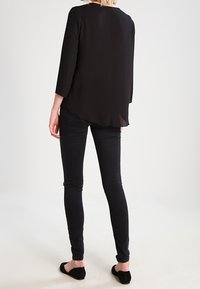 Blusa nera a maniche lunghe con schiena trasparente, abbinata a jeans skinny neri e scarpe platee. La blusa presenta un collo rotondo e un orlo lungo.