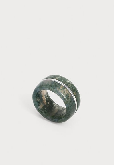 Large bague en agate mousse verte avec une bande lisse en argent encerclant son centre sur un fond clair uni.
