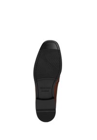Semelle en caoutchouc noir avec des motifs de grip texturés, reliée à un dessus en cuir marron. Les marquages incluent "WITTCHEN" et "fait main."