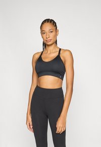 Zwarte sportbeha met brede bandjes, gladde textuur en een aansluitend ontwerp. Gecombineerd met bijpassende zwarte leggings met hoge taille.