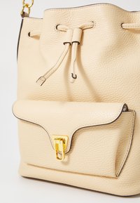 Baldarinväska i texturerat beige läder med dragsnörning, med en framficka och detaljer i guld.
