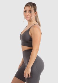 Graues Sportset, bestehend aus einem enganliegenden BH mit dünnen Trägern und hoch taillierten Shorts, beide aus glattem, elastischem Stoff.