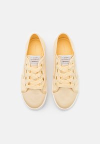 Helle gelbe Leinenschuhe mit weißen Gummisohlen, ausgestattet mit vier Paar Ösen und einer strukturierten Oberfläche. Markenlabel sichtbar auf der Zunge.