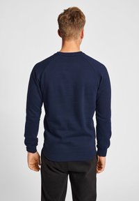 Marineblauwe sweater met lange raglanmouwen, geribde manchetten en zoom, en een zachte textuur. De achterkant toont een klassiek rond decolleté ontwerp.