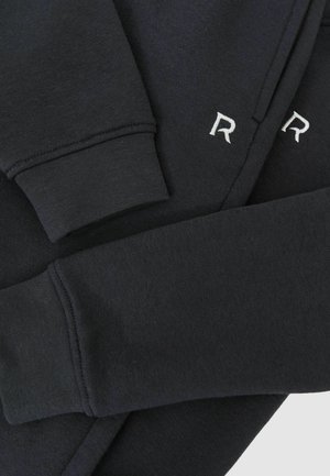 Juodas džemperis su įmegztomis rankovėmis ir siuvinėtu "R.". Pasirinkta minkšta, tekstūrinė medžiaga su švariu, moderniu dizainu.