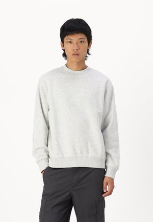 Grå sweatshirt laget av fleece-stoff, har rund hals, lange ermer og ribbestrikket nederkant. Brukt sammen med svarte cargobukser.
