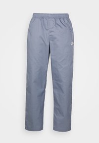 Pantaloni in nylon leggeri e blu con vita elasticizzata e tasche laterali. Presenta un piccolo logo bianco vicino all'anca sinistra. Design a gamba dritta.