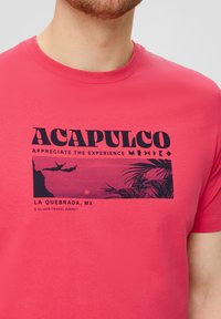 Roze katoenen t-shirt met een retro-stijl graphic featuring "Acapulco," palmbladeren en silhouetten op een zonsondergang achtergrond.