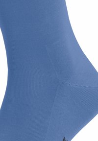 Chaussette bleu clair en tissu texturé lisse. Présente une forme ajustée avec un talon et un orteil renforcés. Détail du logo noir en bas.
