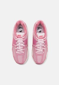 Os ténis Nike Vomero 5 em rosa apresentam um cabedal em malha, língua acolchoada e atacadores. A sola branca contrasta com o design rosa, adicionando textura e detalhe.