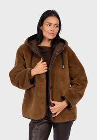 Braune Fleecejacke mit Kapuze, ausgestattet mit einem glatten Innenfutter, schwarzen Kordeln und kontrastierenden Kanten. Sauberes Design mit lockerer Passform.