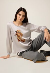 Top grigio chiaro setoso con maniche lunghe e grafica di un cane con un cappello. Abbinato a pantaloni grigi larghi e stivaletti neri alla caviglia. Design minimalista.