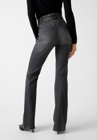 Donkere grijze jeans met wijde pijpen en hoge taille, een nauwsluitende taille, achterzakken en een uniek veterdetail aan de achterkant, gemaakt van denimstof.