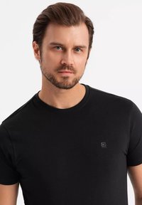 Czarny t-shirt z krótkim rękawem wykonany z miękkiego materiału, z okrągłym dekoltem i małym logo na piersi. Gładka tekstura i dopasowany krój.