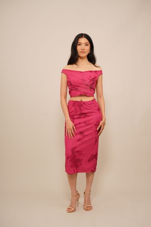 Completo fucsia a due pezzi caratterizzato da un crop top scollato con drappeggi e una gonna liscia fino al ginocchio. Finitura in satin, design elegante.