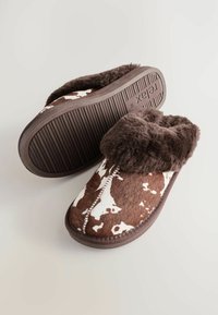 Braune und cremefarbene Kuhflecken-Slipper mit einem weichen Fellkragen, rutschfester Gummisohle und gerippter Textur für Grip und Komfort.