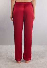 Rode satijnen pyjamabroek met een losvallende pasvorm, een elastische tailleband en omgeslagen hems. Gladde textuur, lange lengte en minimale ontwerpdetails.