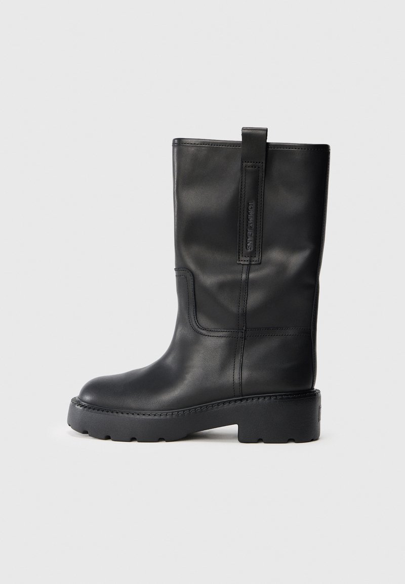 Botas de cuero negras hasta la rodilla con un diseño elegante, que cuentan con una suela gruesa y una pestaña lateral para ponerlas con facilidad. Destacan los acentos de costura.