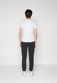 Hvit kortermet t-skjorte kombinert med svarte joggebukser, som har en tettsittende passform og mansjetter. Skoene er hvite sneakers med grå detaljer.
