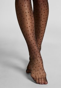Zwarte doorschijnende panty met een stippenpatroon van kleine donkere stippen. Vlotte textuur, getailleerd ontwerp en open teen detail zichtbaar.