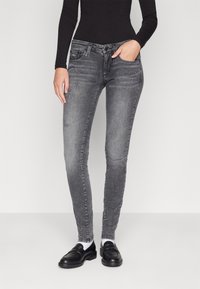 Jeans de mezclilla gris de corte ajustado con detalles desgastados, diseño de cinco bolsillos y pasadores para cinturón; combinados con mocasines negros y calcetines blancos.