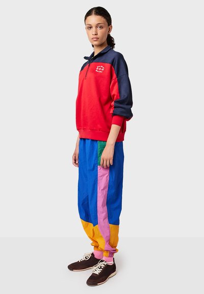 Red and navy zip-up sweatshirt, paired with blue, pink, green, and yellow color-blocked pants. Features elastic cuffs and sporty design.