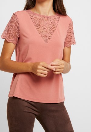 Blush pink top with a V-neck and lace short sleeves. Soft texture, relaxed fit, and detailed lace pattern at the neckline and sleeves.