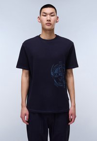Marineblå bomulds t-shirt med et tekstureret cirkulært grafisk motiv på forsiden. Korte ærmer og en afslappet pasform med en rund halsudskæring.