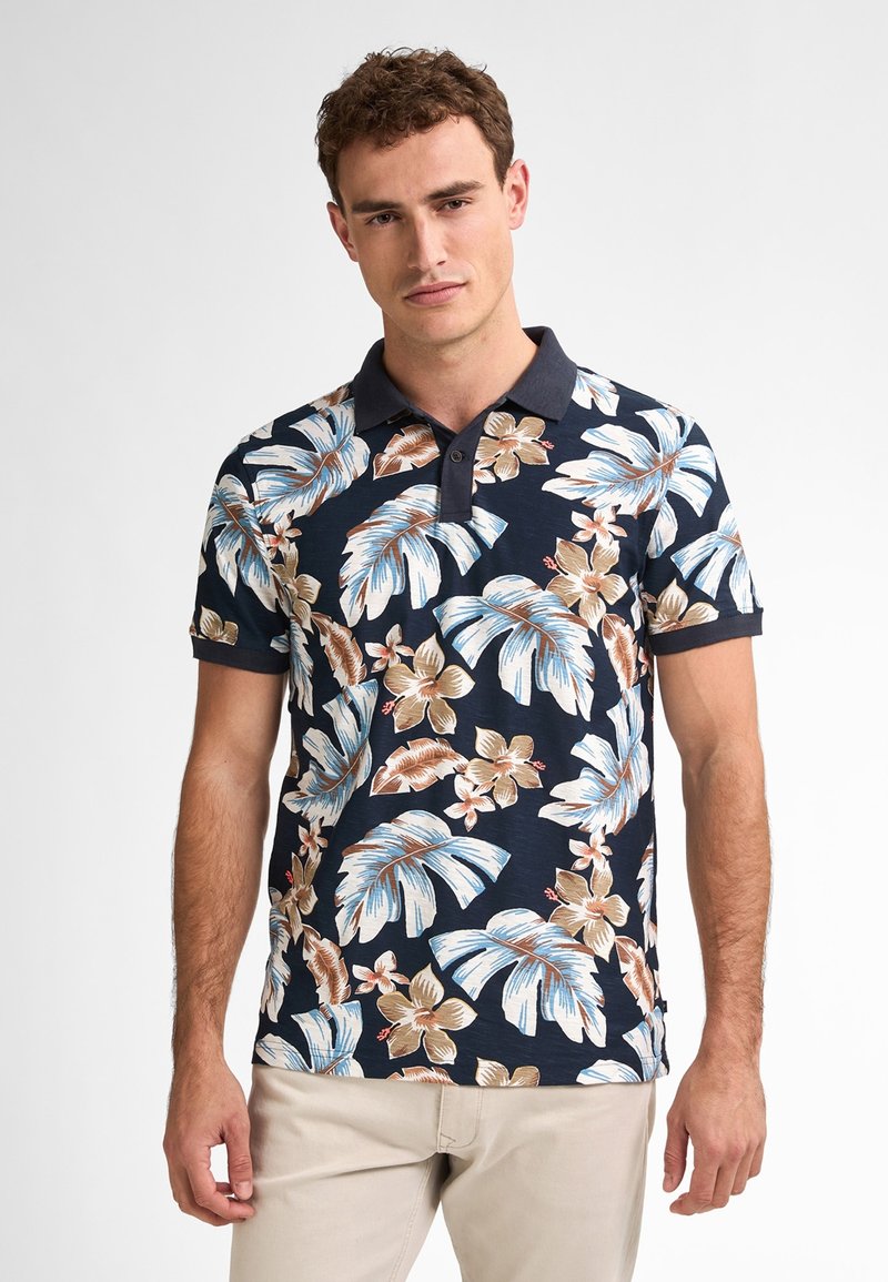 Polo color azul marino con un estampado floral que presenta grandes hojas y flores en tonos beige, marrón y azul claro. Mangas cortas y un collar de contraste.