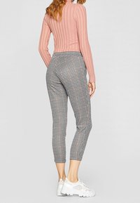 Pantalons cropped à carreaux en noir, blanc et gris, associés à un haut ajusté en rose côtelé et des baskets de sport blanches.