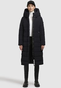 Cappotto imbottito navy con texture trapuntata, colletto alto e cappuccio staccabile. Presenta tasche con zip e dettaglio del logo sull'orlo.