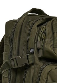 Olive zaļā taktiskā mugursoma ar vairākiem rāvējslēdzējiem, teksturētu audumu, regulējamām siksnām un plastmasas sprādzi.