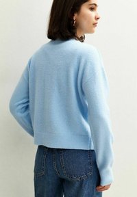 Pull court bleu clair en tissu doux, avec un col rond et un ourlet côtelé, associé à un jean en denim taille haute.