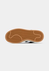 Svart-hvitt joggesko med såle av gummigummi som har et sikksakkmønster og glatt tekstur. Minimalistisk design med tre striper.