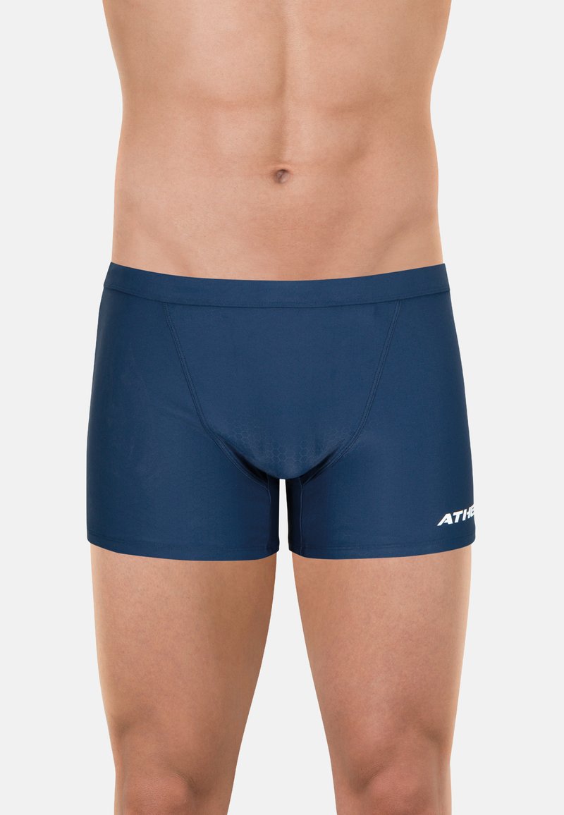 Shorts de bain bleu marine en tissu extensible, avec une coupe ajustée, une texture lisse, et un motif hexagonal à l'avant. Logo affiché sur le côté.