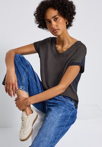 T-shirt à col en V avec un devant à motifs foncés et des côtés bleu marine, associé à un jean baggy bleu et des baskets texturées beiges.