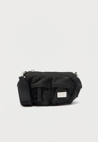 Svart nylon skulderveske med to lommer foran, sølvglidelås og en avtakbar stropp. Har en liten logodetalj på siden.