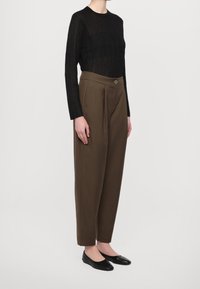 Svart långärmad topp med ribbad textur, kombinerad med högmidjade, bruna veckade byxor med en knapp framtill och tapered ben, svarta lägenheter.