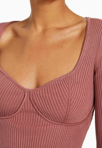 Geripptes Langarmshirt in Mauve mit weitem, abgerundetem Ausschnitt und auffälligen Nahtdetails über der Brust und unter dem Ausschnitt.