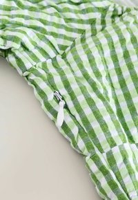 Zeleno-bílá kostkovaná látka s texturovaným povrchem, na boku s bílým zipem. Design má na švu nařasený detail.