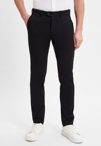 Black trousers made of textured fabric, featuring a button closure and side pockets, paired with white sneakers for a casual look.