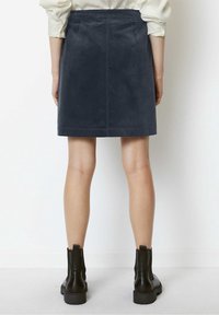 Gonna mini in suede blu navy con tasche posteriori, taglio dritto e dettagli di cucitura, abbinata a stivali neri alla caviglia e gambe nude visibili.