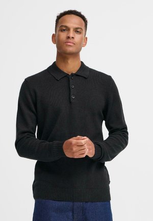 Camisa de polo de punto negro con puños y dobladillo acanalados, que presenta una tapeta de tres botones y un collar estándar. Corte casual y tejido texturizado.
