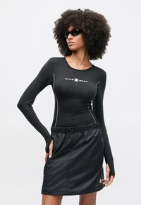 Čierne športové tričko s dlhým rukávom a priliehavým strihom s bielymi prúžkami, doplnené o čiernu sukňu s elastickým pásom, bočným vreckom a detailom s logom.