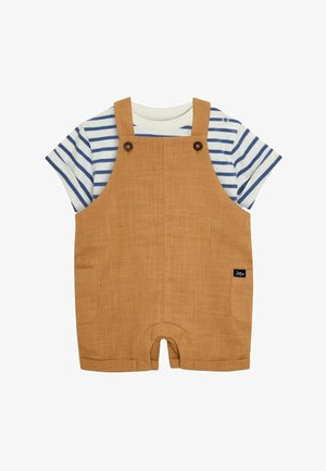 Beige Latzhose aus strukturiertem Stoff, mit zwei seitlichen Knöpfen, einer Tasche und einem dunkelblauen Logo-Tag, darüber ein blau-weiß gestreiftes T-Shirt.